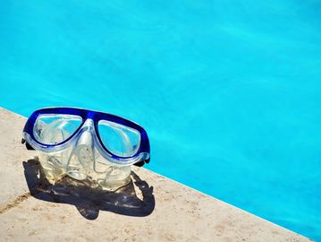 Diving mask resting on the edge of a bright blue swimming pool.