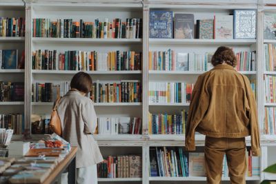 Two people browsing books on white shelves in a bookstore.