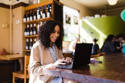 Woman sat at a table smiling at her laptop which is open in front of her on the table.