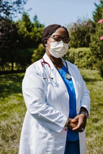 Female doctor wearing a white coat and mask outdoors.