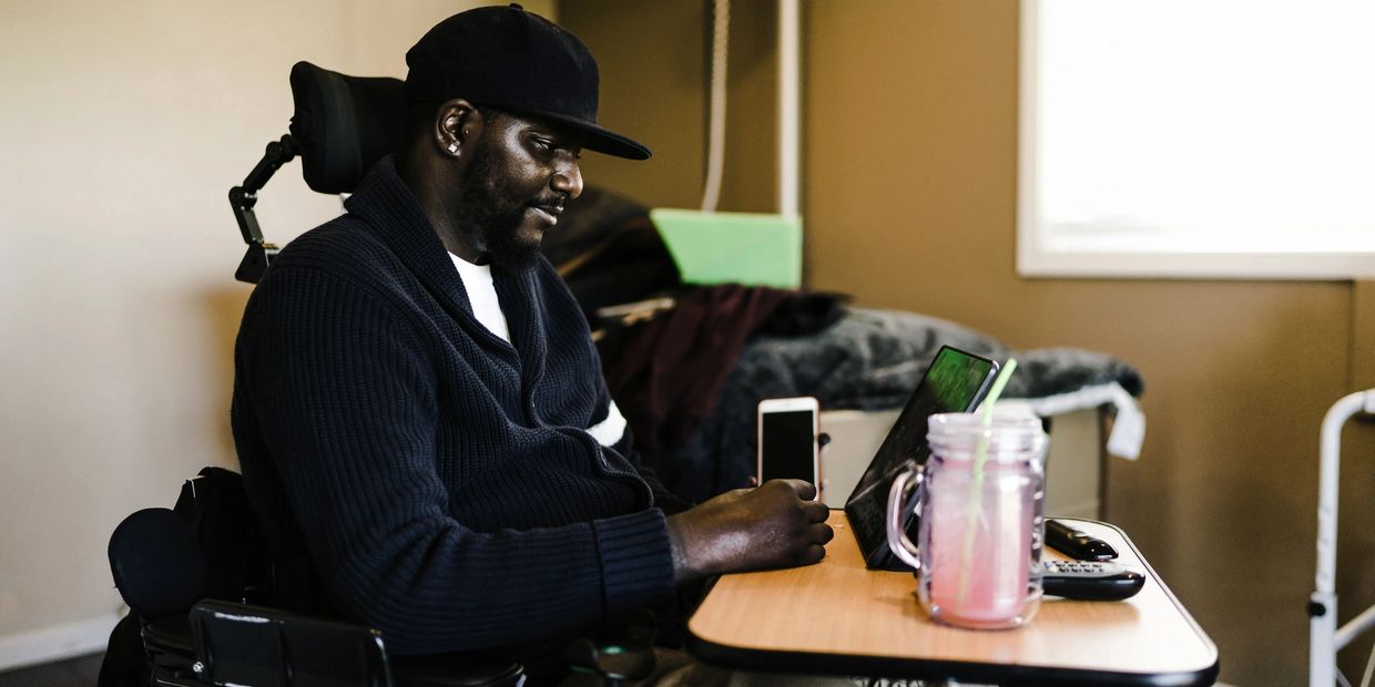Man in a wheelchair at a desk indoors, using a smartphone.