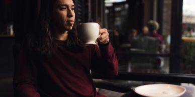 A person in a maroon sweater sipping from a white cup in a cozy cafe.