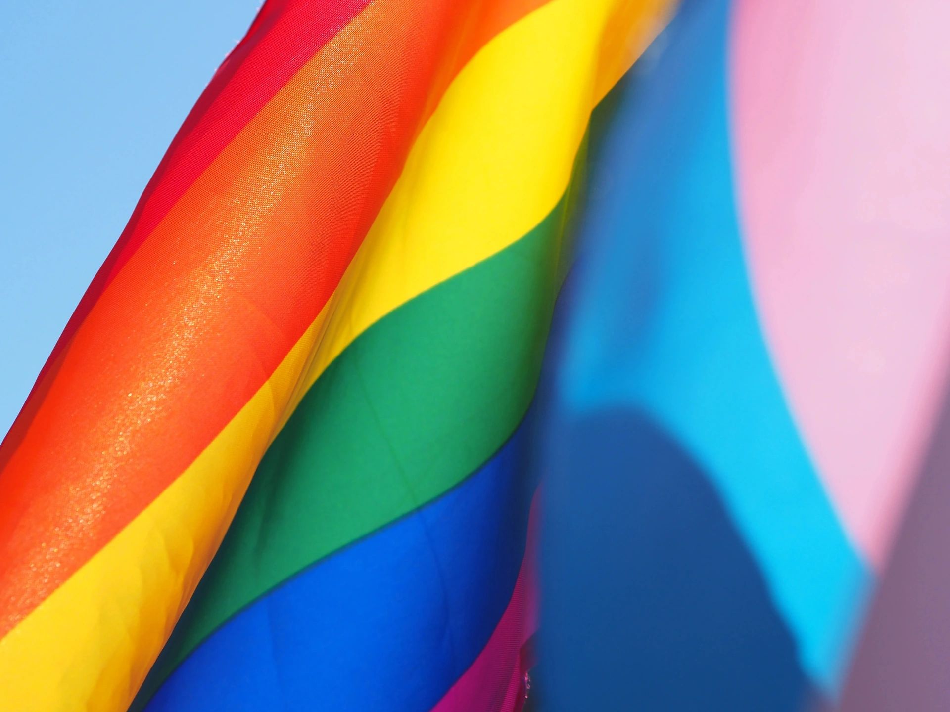 Close-up of a waving rainbow pride flag against a clear blue sky.