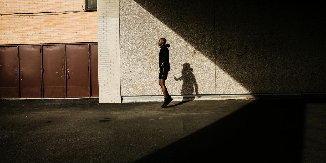 A man jumping rope casting a shadow on a wall with angled sunlight.