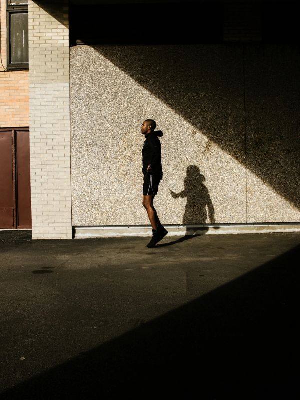 Man jumping rope outdoors casting shadow on wall.
