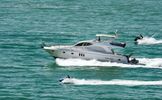 A luxury yacht speeding through the ocean with people on jet skis nearby.