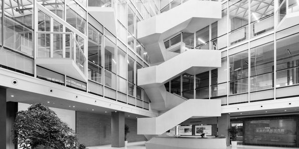 Modern office lobby with geometric staircase and glass walls.