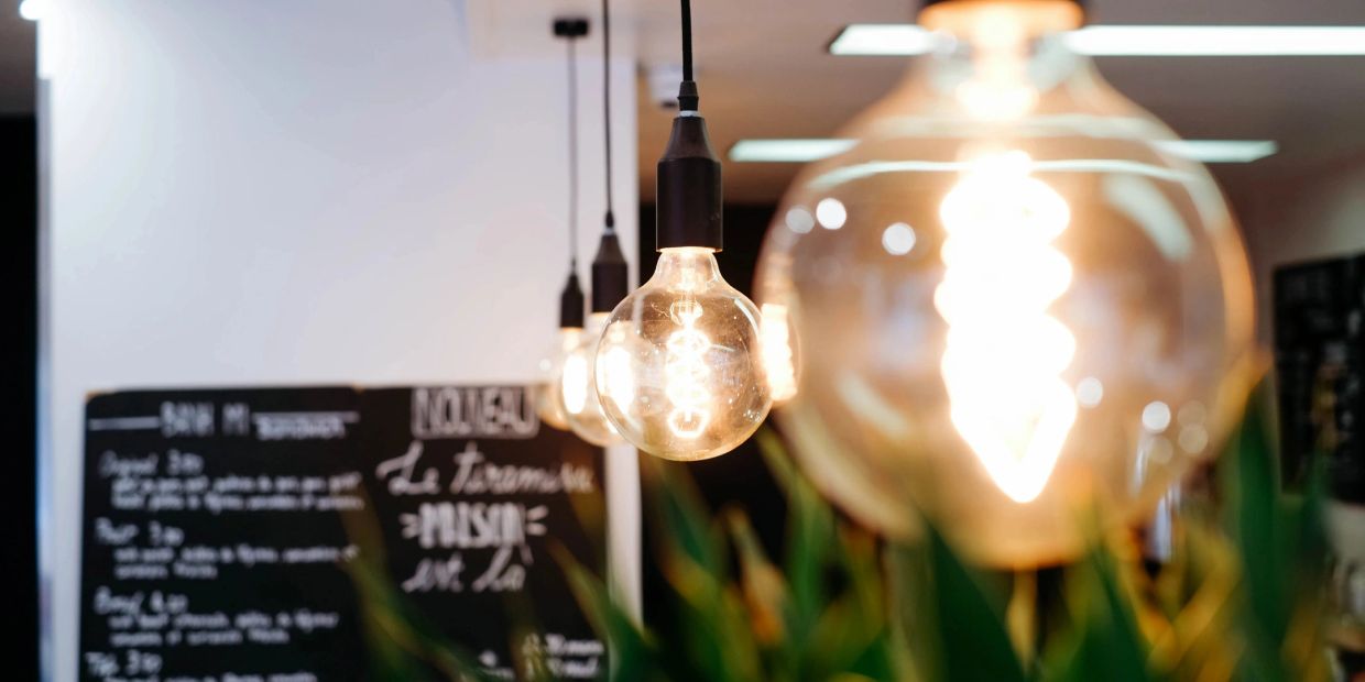 A row of vintage-style hanging light bulbs glowing warmly in a cozy cafe.