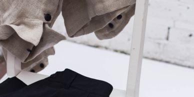 Beige buttoned jacket hanging over a white chair with black pants below.