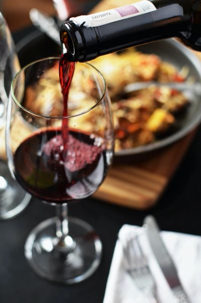 Red wine being poured into a glass with food in the background.