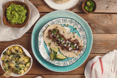 Two tacos with chopped meat and onion on a decorative plate.