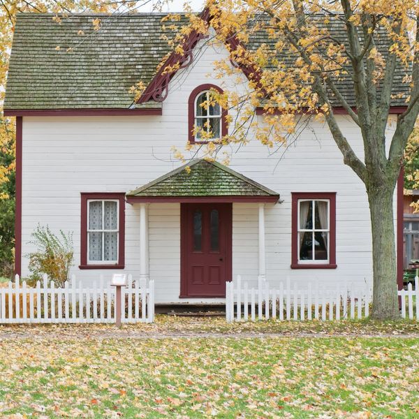 Cozy white house with red door and autumn leaves.