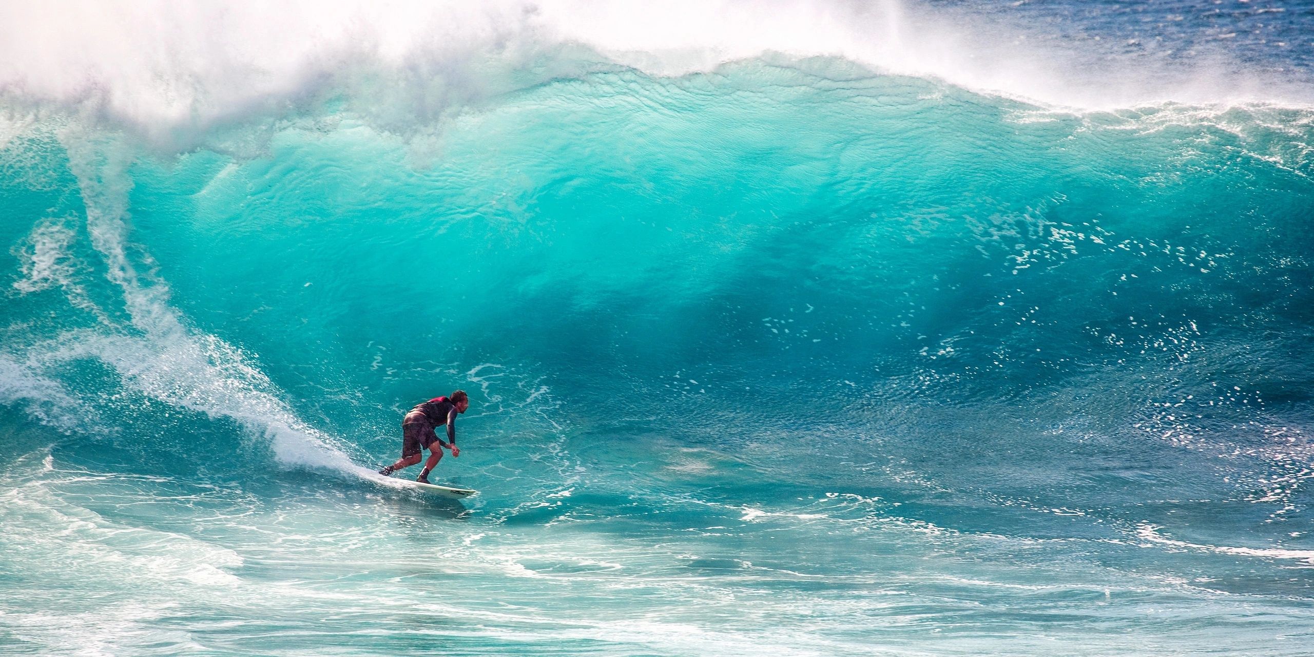 Person surfing on turquoise giant wave