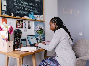 Woman working on a laptop at a decorated desk in a cozy room.