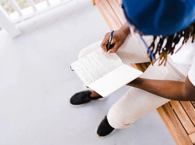 Person writing in a notebook on a bench.