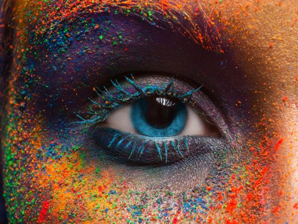 Close-up of a blue eye with colorful paint on the skin.