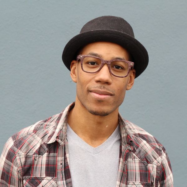 Man wearing glasses, a black hat, and a plaid shirt against a gray background.