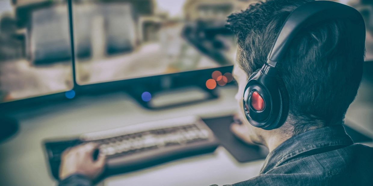 Man wearing headphones using a computer with dual monitors.