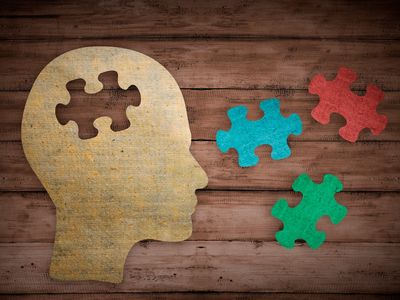 profile silhouette of wooden model of head with empty puzzle piece shape next to other puzzle pieces