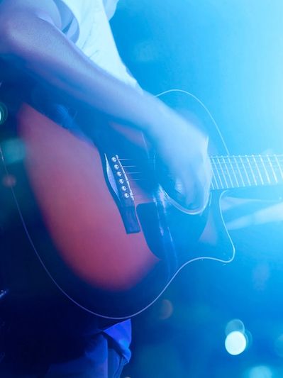 A person playing an acoustic guitar on stage with blue lighting.
