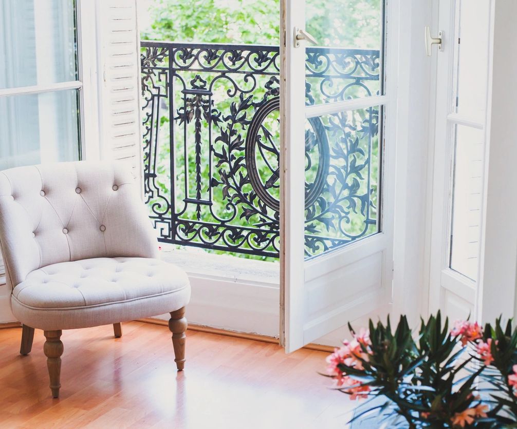 Bright room with a tufted chair, open balcony door, and floral plant.