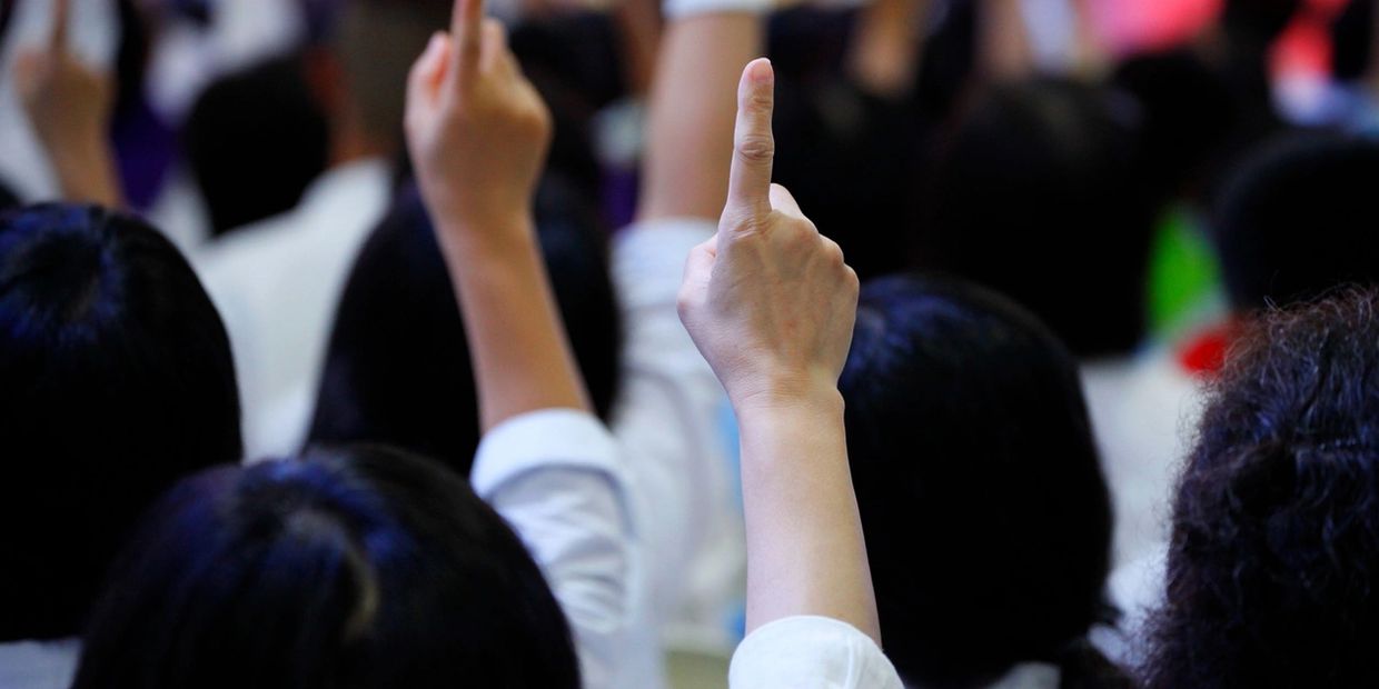 People raising their index fingers in a crowd, possibly signaling participation.