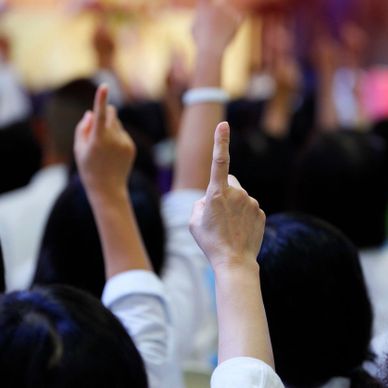 Raised hands with index fingers pointing up in a crowd.