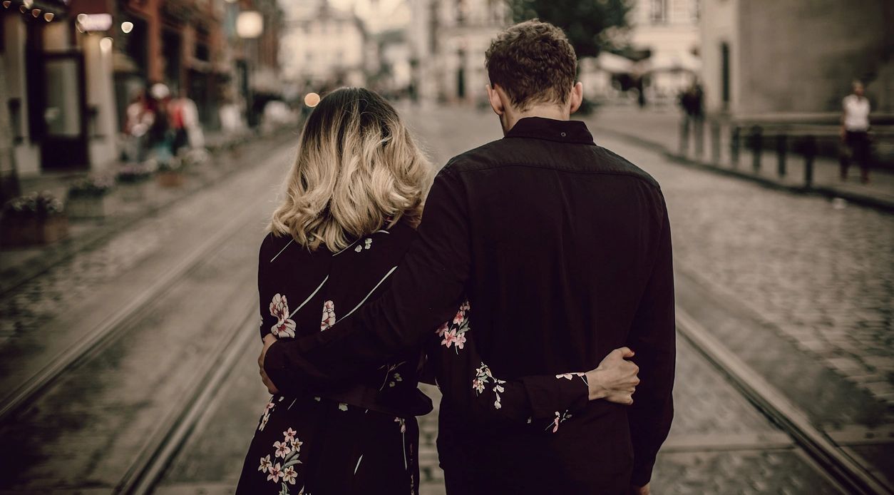 Couple walking arm in arm down a cobblestone street.