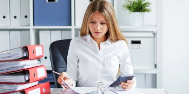 Auditor holding a calculator, reviewing records, and examining a pile of documents on her desk