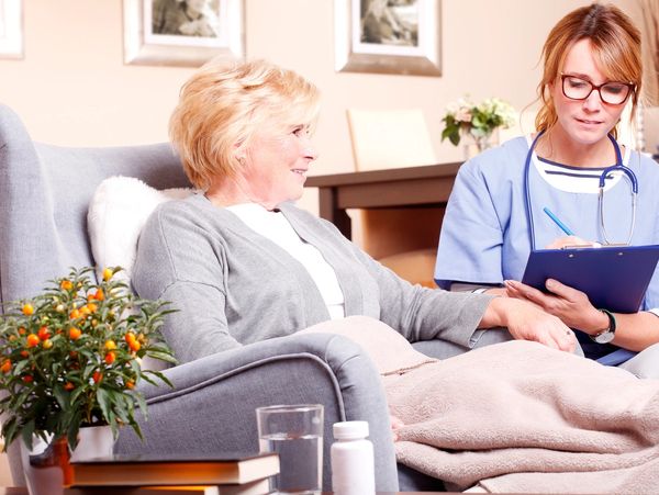 A nurse attentively consulting with an elderly woman in a cozy living room setting.