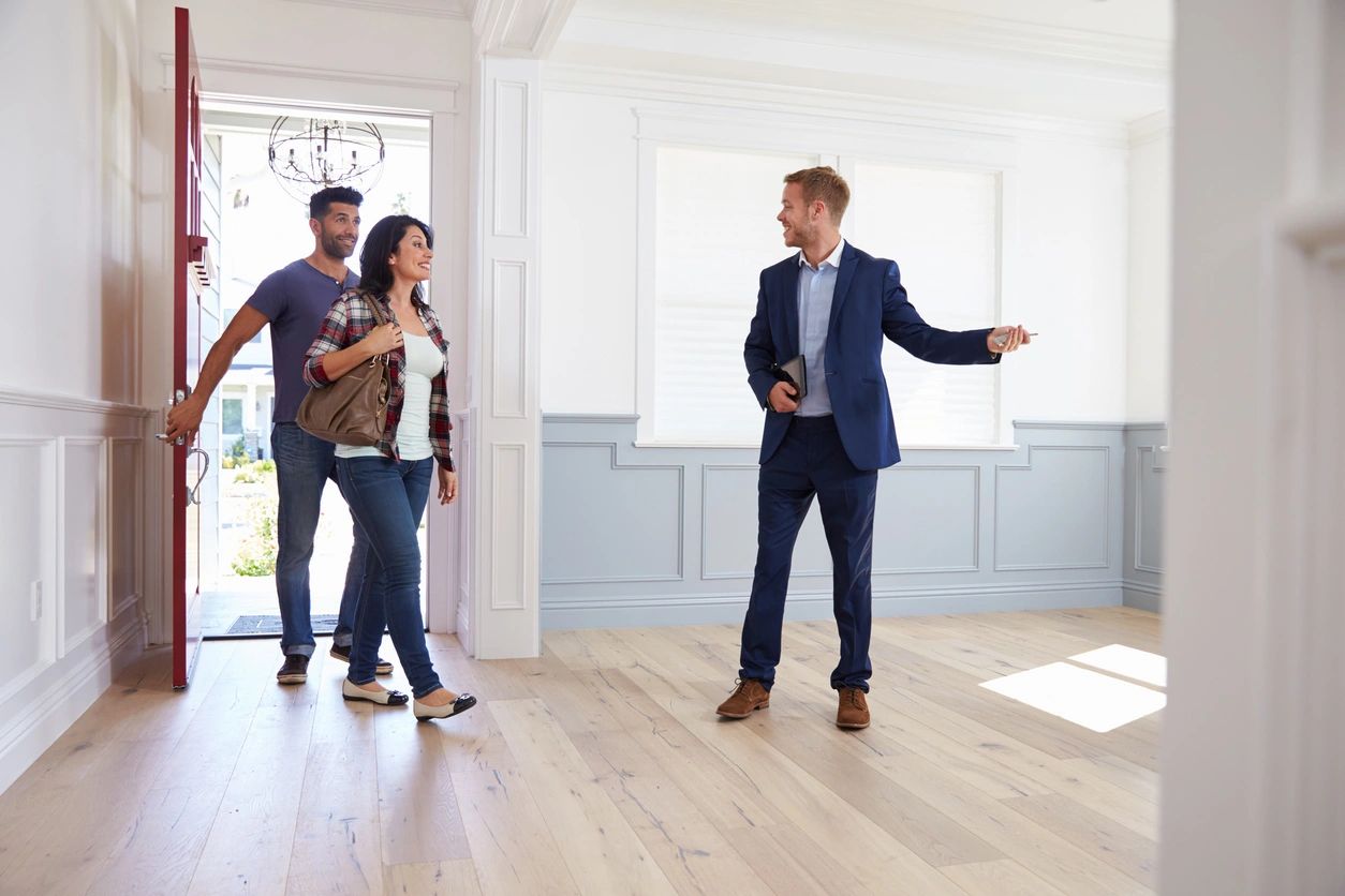 Realtor leads the way as he shows the two potential home buyers a new home as they enter the house.