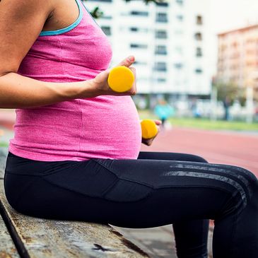 Pregnant woman exercising with small dumbbells outdoors.