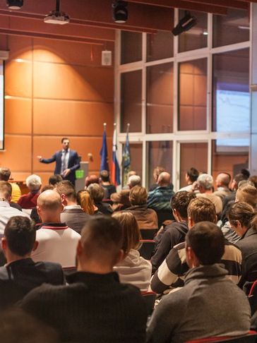 A speaker presenting to a large audience in a conference room.