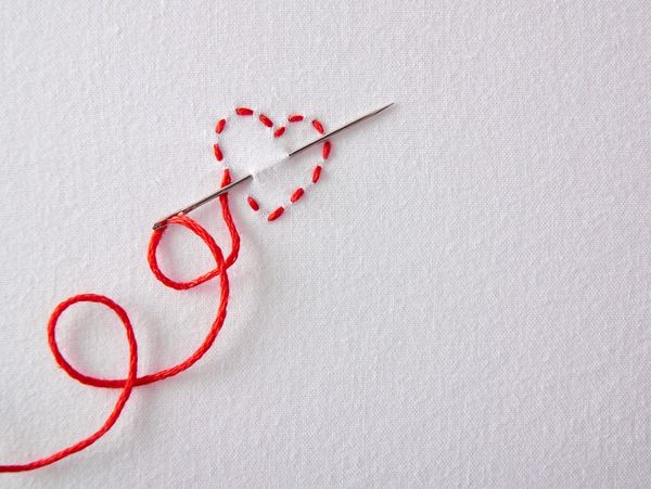 A needle with red thread stitching a heart shape on white fabric.