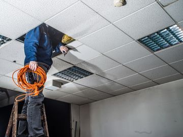 man looking in drop ceiling on ladder