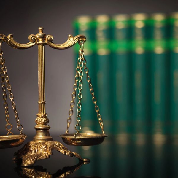 Depicting a Law Office, a set of law reference books behind a set of brass scales of justice.