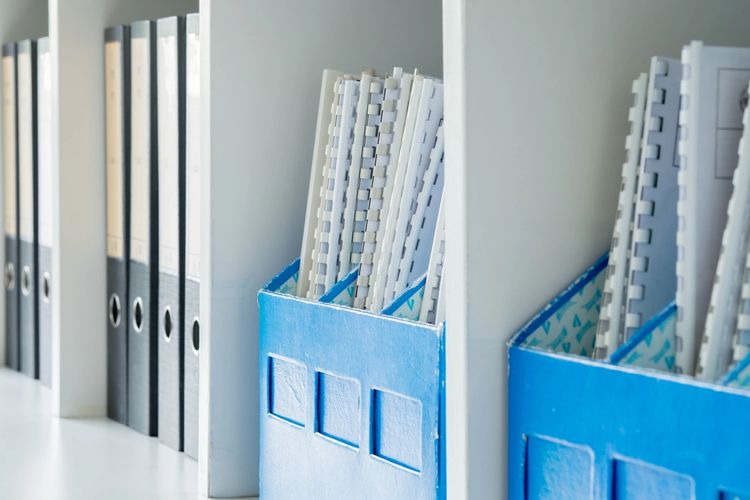 Organized office shelves with binders and blue file holders.