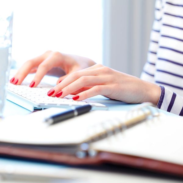 Hands typing on a keyboard with a notebook and pen nearby.