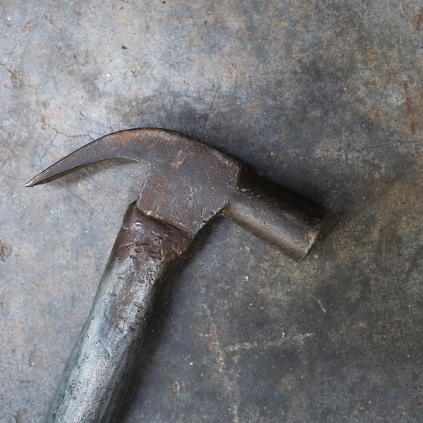 Old rusty hammer with a worn metal handle on a concrete floor.