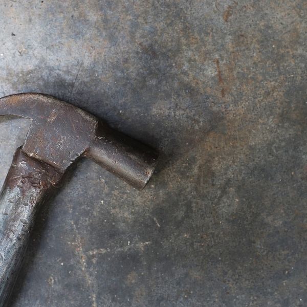 Old rusty hammer with a worn metal handle on a concrete floor.
