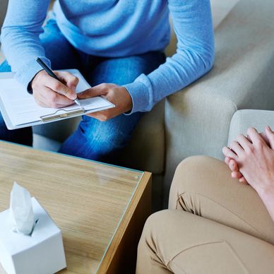A therapy session with a counselor taking notes and a patient sitting anxiously.