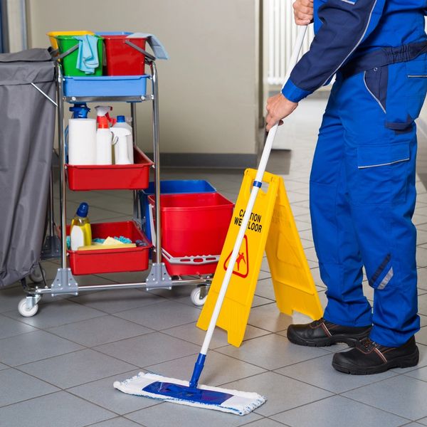 Janitor mopping floor near cleaning cart and caution sign.