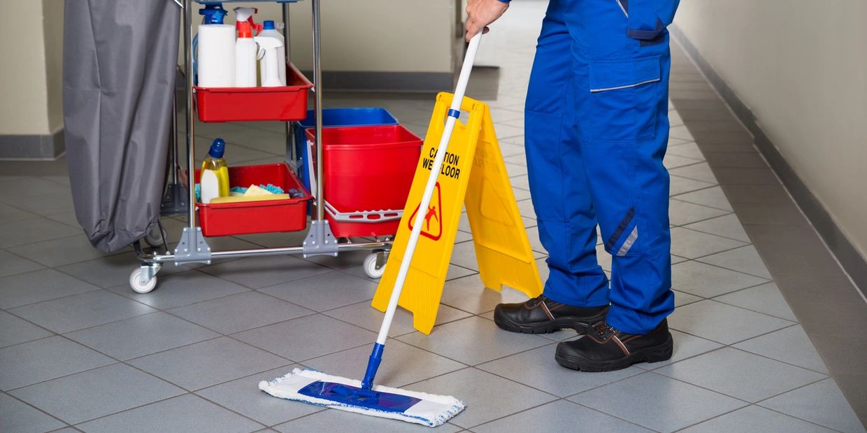 Janitor mopping the floor near a caution sign and cleaning cart.
