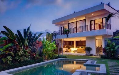 Modern two-story house with a pool and tropical landscaping at dusk.