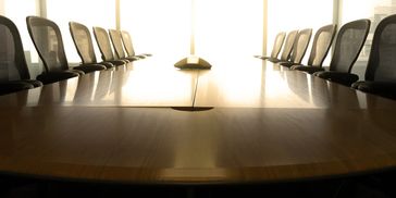 Empty conference room with a polished wooden table and mesh chairs.