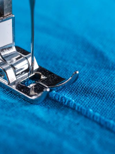 Close-up of a sewing machine needle stitching blue fabric.