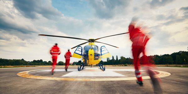 Emergency responders rush to a yellow rescue helicopter on a helipad.