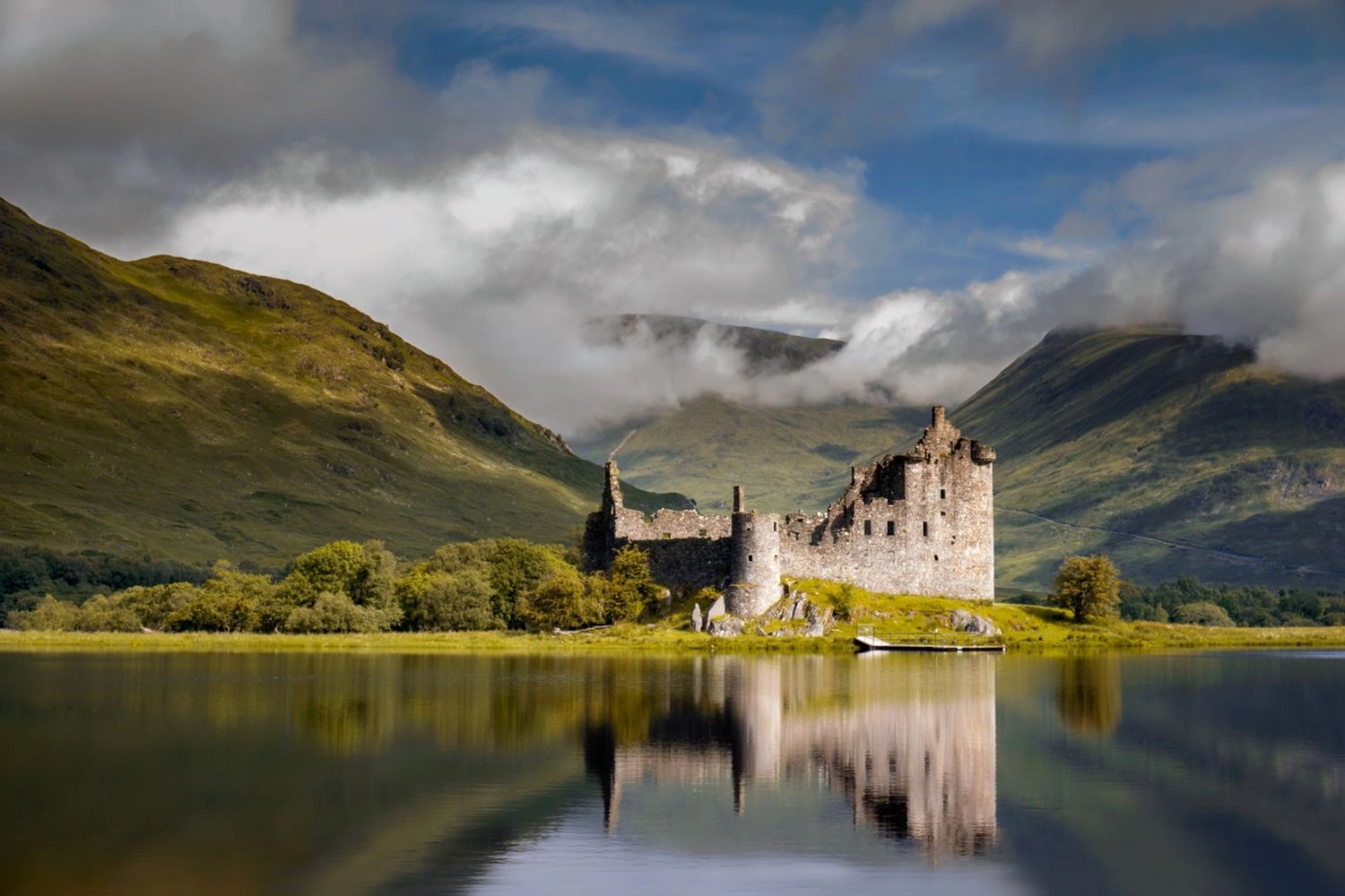 Scottish loch-side castle with backdrop of mountains and whispy white clouds