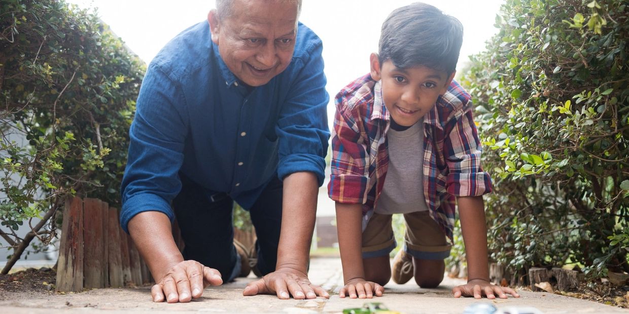 Grandfather and grandson playing with toy cars outside on a sunny day.