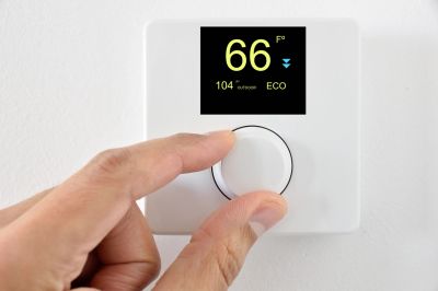 Hand adjusting a smart thermostat set to 66°F.